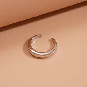 Gros plan d'une bague ouverte en forme de C argentée sur fond rose courbé doux