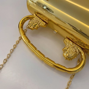 Detail of the golden metal evening bag featuring an embossed lion head handle and chain