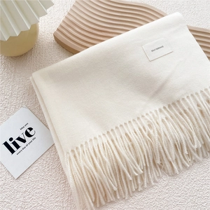 Close-up of cream white scarf with tassels and minimalist woven label on textured background