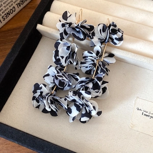 Close-up of elegant black and white floral drop earrings with a stylish cow print fabric