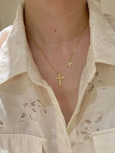 Close-up of a 24K gold plated cross necklace with small charms on a lace shirt