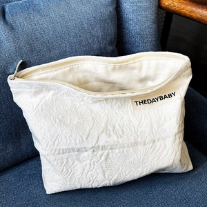 Detail of white textured floral jacquard fabric and beige zipper on portable cosmetic bag