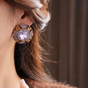 Close-up of vintage style round earring with purple gemstone and pink crystals on model