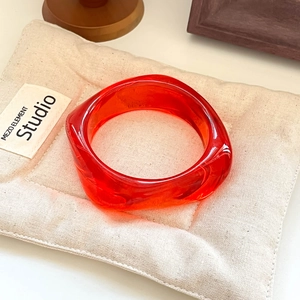 Macro shot of a red transparent resin wide cuff bracelet on a beige linen mat
