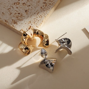 Detail of minimalist gold and silver twisted C-shape metal earrings on stone