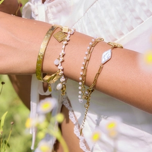 Gold layered bracelet set featuring pearls and charms on model in sunny outdoor setting