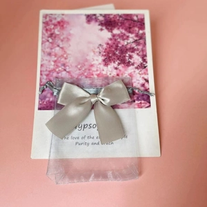 Detail of light gray organza gift bag with ribbon bow on floral background