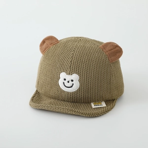 Détail du bonnet en velours pour bébé avec oreilles d'ours et patch brodé souriant