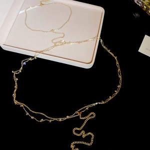 Detail of delicate gold body chain with zircon beads and fringes on a white jewelry tray