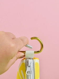Detail showing the golden carabiner hook and zipper of the fruit print pet bag dispenser