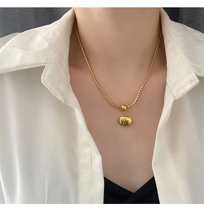 Close-up of minimalist gold box chain with polished bean pendant on a white shirt