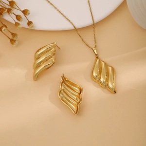 Detailed view of golden luxury jewelry set with abstract wavy leaf patterns on a warm base