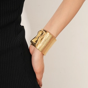 Detail view of gold wide cuff bracelet with linear texture on a model's wrist