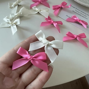 Pink and white satin bow hair clips in balletcore style shown on a hand and table