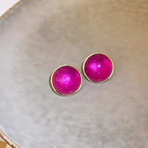 Close-up of magenta round stud earrings with golden metal borders on a gray ceramic plate