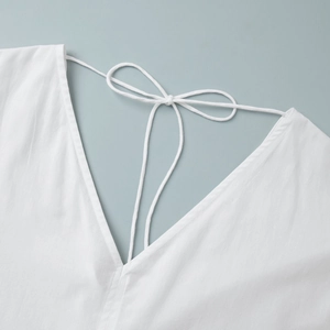Close-up of V-neckline with delicate bow tie strings on a white cotton dress