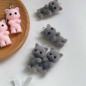 Close-up of pink and grey flocked kitten charms with metal rings on white leather background