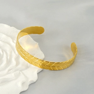 Detailed macro view of 18K gold-plated stainless steel bangle with wheat grain pattern