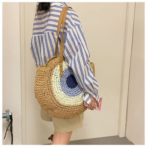 Detail of handwoven straw tote bag with evil eye pattern and brown leather straps