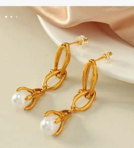 Detail view of a long gold chain earring with a round pearl drop on silk fabric