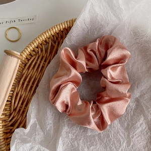 Macro shot of peach satin scrunchie showing glossy silk texture and pleated elastic design