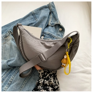 Close-up of gray nylon crescent bag with adjustable strap and yellow penguin charm accessory