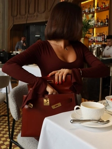 Detail of burgundy leather Kelly style handbag with gold hardware and clover necklace
