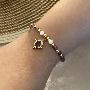 Beaded bracelet with purple natural stones and gold pendant worn on wrist outdoors