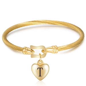 Detail of twisted 18K gold horseshoe bangle with heart pendant featuring engraved letter T