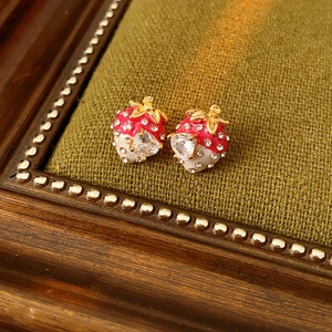 Detail view of strawberry earrings with red enamel and crystals on green fabric background