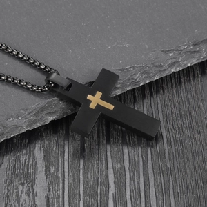 Detail of black stainless steel cross pendant with gold inlay on dark wood background