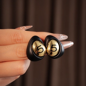 Detail of a vintage-style gold-plated earring with a black frame and number 5 design