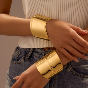 Minimalist wide gold-finish irregular metal cuff bracelet worn by a model in casual style