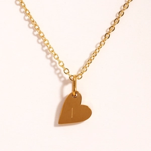 Détail d'un collier pendentif cœur doré avec la lettre I gravée sur fond blanc