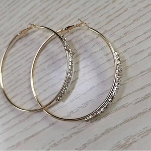 Minimalist large gold hoop earrings with clear rhinestones on light wood grain surface