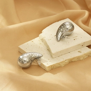 Close-up of silver teardrop earrings with hammered texture on beige stone and silk background