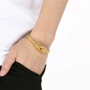 Close-up of golden knotted metal cuff bracelet with realistic rope texture detail on wrist