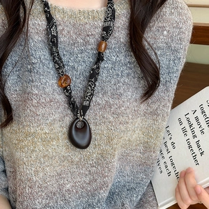 Ethnic necklace with dark brown pendant and black fabric cord on a grey knit sweater