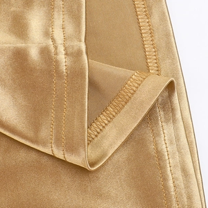 Macro detail of high-shine gold satin fabric with precise overlock stitching seams