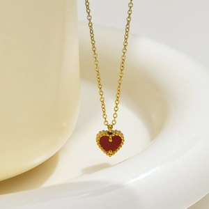 Dettaglio della collana dorata con pendente a cuore rosso e bordo con perline