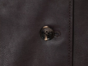 Close-up of brown button and stitching on high-quality faux leather stand collar jacket