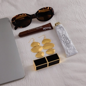 Flatlay de boucles d'oreilles géométriques dorées étagées sur tissu blanc avec accessoires