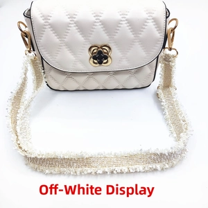Detail of off-white quilted shoulder strap with clover buckle and tassel accent