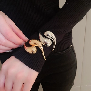 Polished gold and silver waterdrop bangles worn over black pleated sleeves