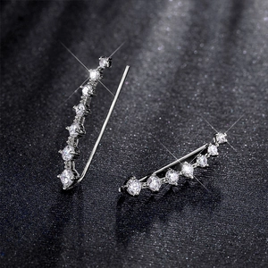 Macro shot of silver ear climbers with sparkling zircon stones on dark background