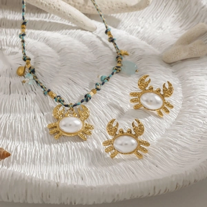 Goldenes Krebs-Schmuckset mit blauer Webhalskette und Perlenohrringen auf Muschel