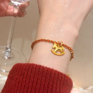 Détail macro du charm cheval à bascule plaqué or 24K sur un bracelet en corde tressée rouge