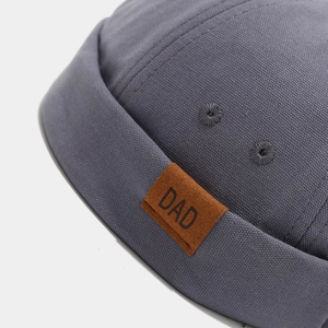Détail d'un bonnet docker gris foncé avec un écusson en daim marron et lettrage DAD