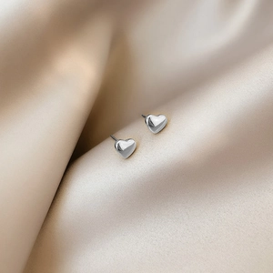 Polierte silberne Herzstecker, elegant auf champagnerfarbenem Seidenstoff präsentiert