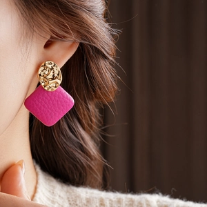 Close-up of golden irregular hammered metal and rose red square leather drop earrings